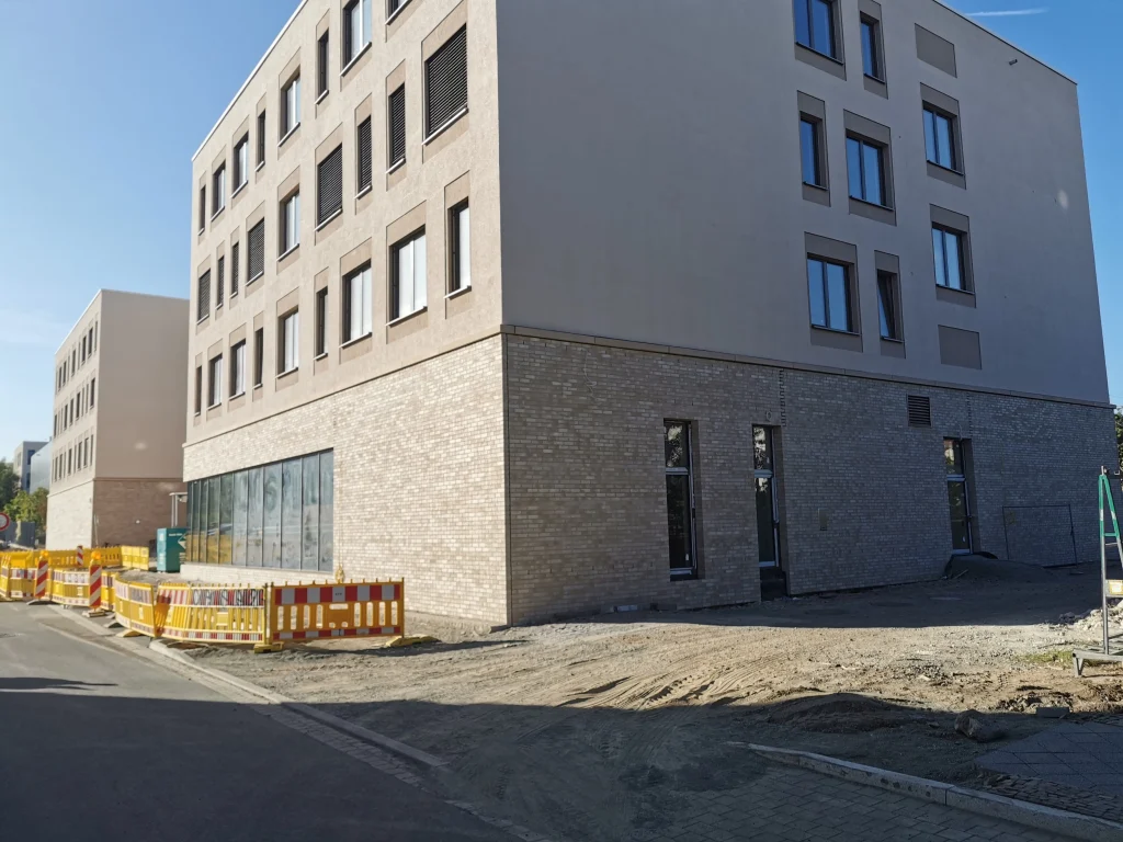 Außenansicht eines Neubaus mit Klinkerfassade und Baustellenabsperrungen im Vordergrund.